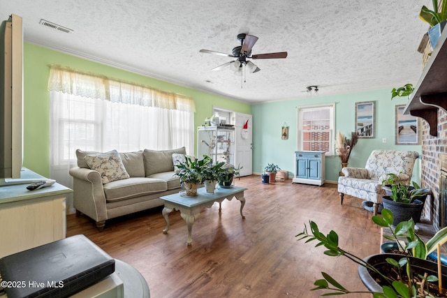 living room featuring a textured ceiling, visible vents, crown molding, ceiling fan, and wood finished floors