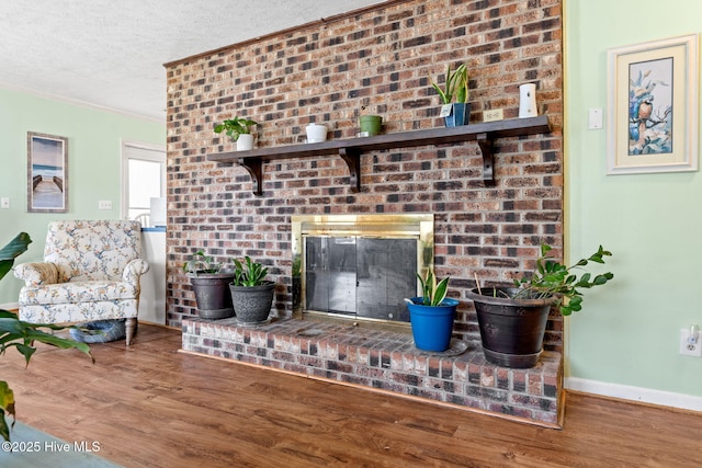 living area featuring a textured ceiling, a brick fireplace, baseboards, ornamental molding, and wood finished floors
