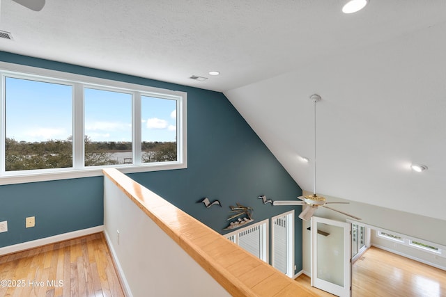 corridor with an upstairs landing, lofted ceiling, light wood-style flooring, baseboards, and visible vents