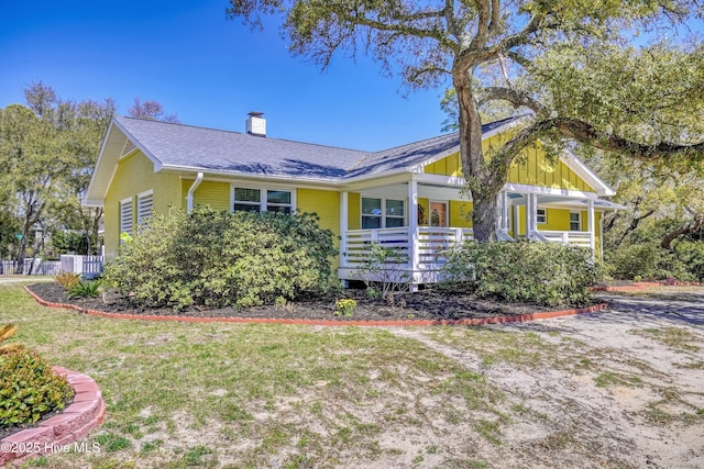 302 NE 60th St, Oak Island, NC 28465 - view of side of home featuring covered porch, a chimney, a yard, and board and batten siding