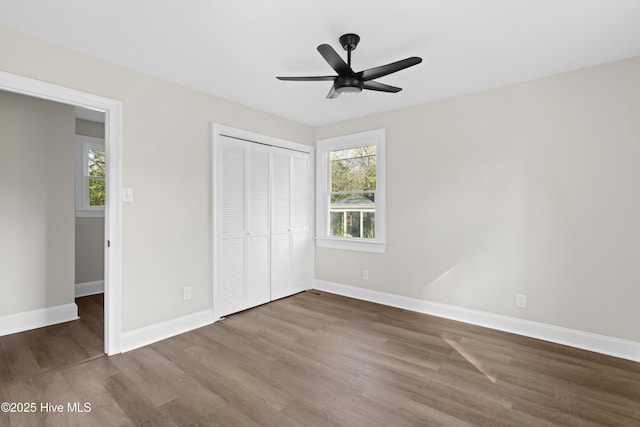 unfurnished bedroom with baseboards, multiple windows, dark wood-type flooring, and a closet