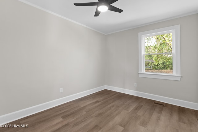 spare room with ceiling fan, dark wood finished floors, baseboards, ornamental molding, and visible vents