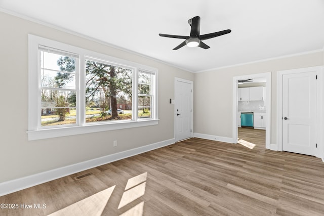 interior space with a ceiling fan, wood finished floors, baseboards, ornamental molding, and visible vents