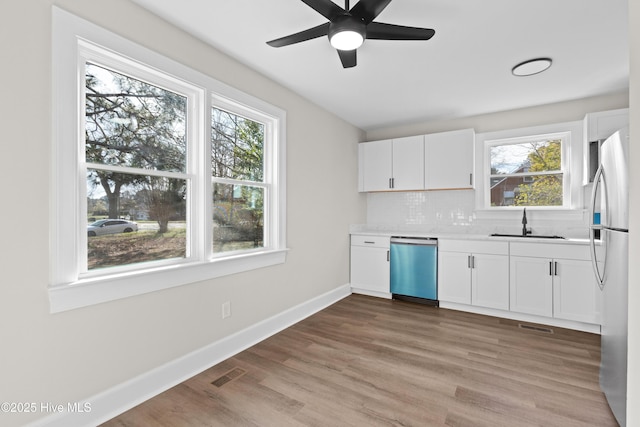 kitchen with a sink, dishwashing machine, white cabinets, visible vents, and freestanding refrigerator