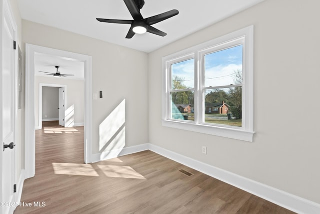 spare room featuring light wood finished floors, a ceiling fan, baseboards, and visible vents