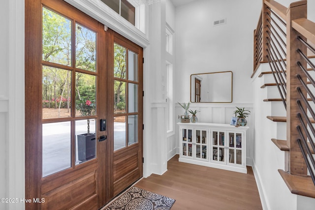 entrance foyer featuring stairway, french doors, visible vents, a decorative wall, and wood finished floors
