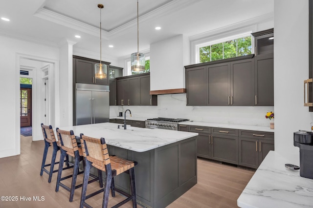 kitchen featuring light wood-type flooring, appliances with stainless steel finishes, crown molding, pendant lighting, and light stone counters