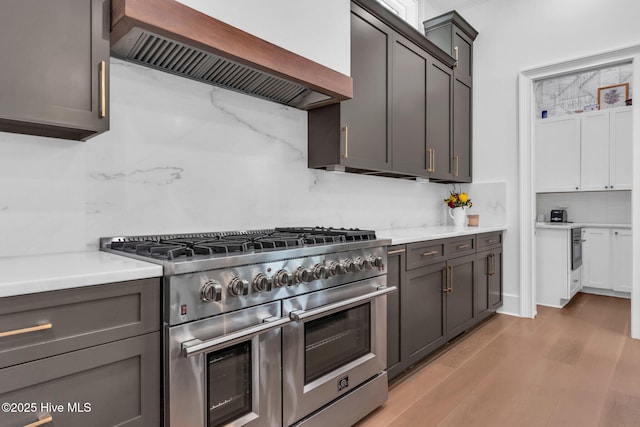 kitchen featuring custom exhaust hood, light wood finished floors, range with two ovens, and tasteful backsplash