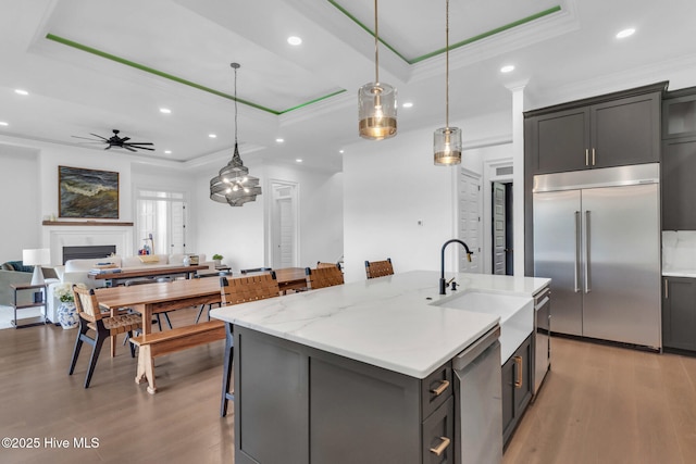 kitchen featuring light wood-type flooring, a fireplace, a tray ceiling, ceiling fan, and appliances with stainless steel finishes