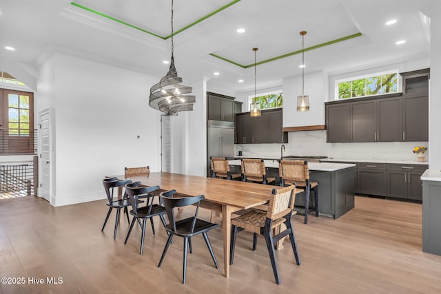 dining area featuring a raised ceiling, light wood-type flooring, ornamental molding, and a wealth of natural light