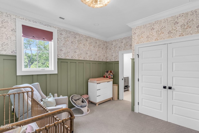 bedroom featuring crown molding, a nursery area, a wainscoted wall, carpet floors, and wallpapered walls