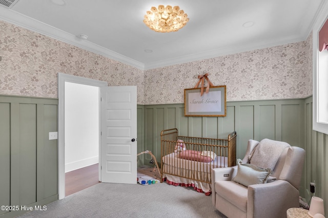 carpeted bedroom with a decorative wall, ornamental molding, wainscoting, a crib, and wallpapered walls