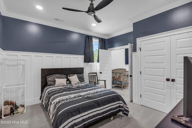 bedroom featuring crown molding, a decorative wall, wainscoting, and carpet floors