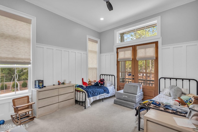 bedroom with french doors, crown molding, wainscoting, a decorative wall, and light colored carpet