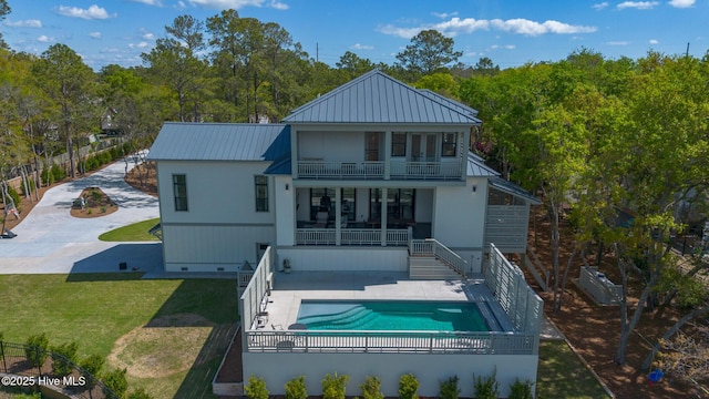 rear view of house featuring a patio, a balcony, a fenced backyard, metal roof, and a lawn