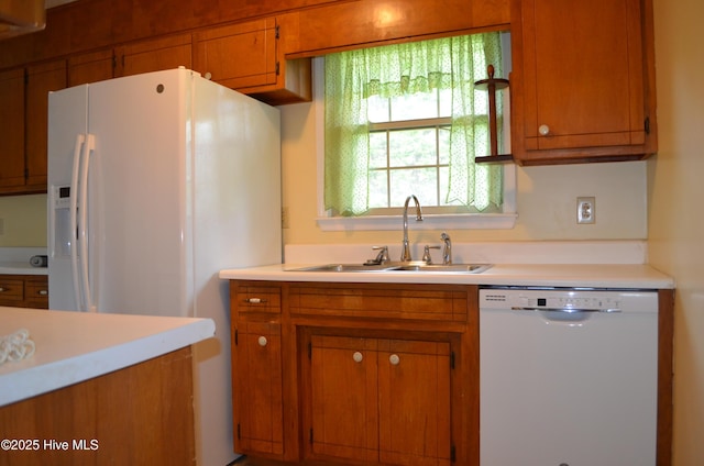 kitchen with brown cabinetry, white appliances, light countertops, and a sink