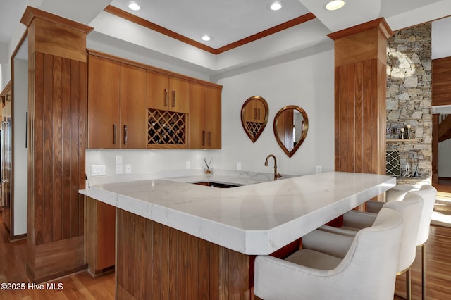 1409 Landfall Dr, Wilmington, NC 28405 - kitchen featuring light wood-style floors, brown cabinetry, light stone counters, a peninsula, and a breakfast bar area