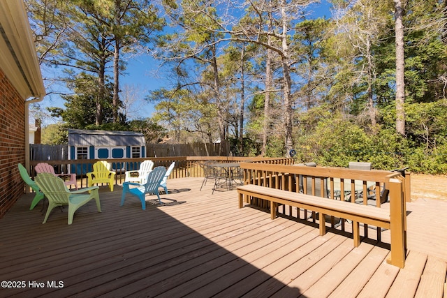 wooden terrace featuring outdoor dining space, a fenced backyard, an outbuilding, and a storage unit