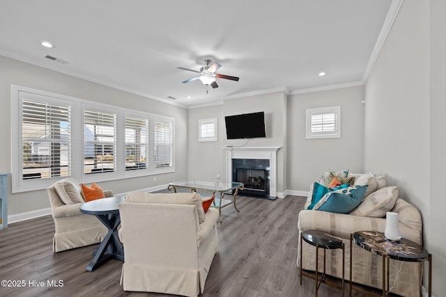 living area featuring wood finished floors, visible vents, a ceiling fan, crown molding, and a fireplace