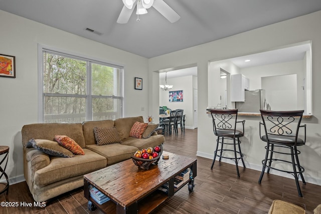 living room with ceiling fan with notable chandelier, visible vents, baseboards, and dark wood-type flooring