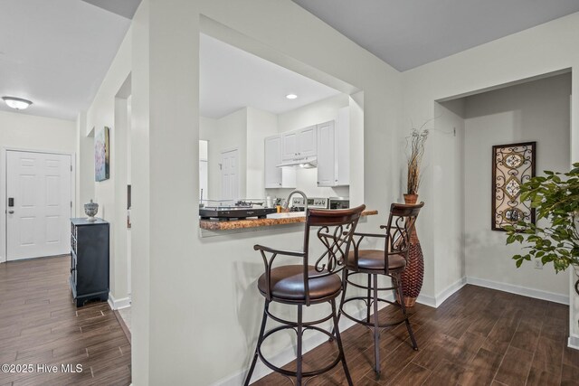 kitchen with baseboards, wood tiled floor, white cabinetry, and a kitchen bar