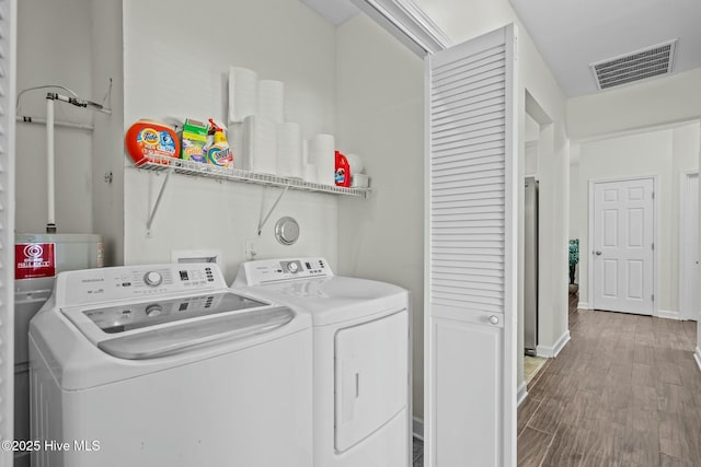 washroom featuring visible vents, baseboards, wood finished floors, laundry area, and washer and clothes dryer