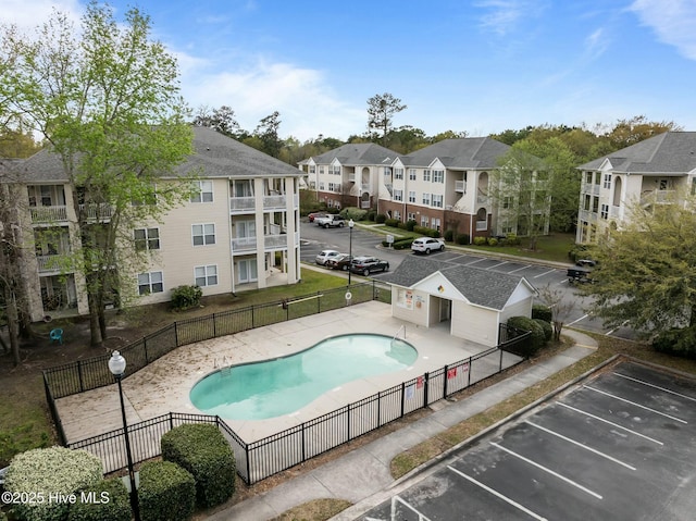 community pool with a patio, fence, and a residential view