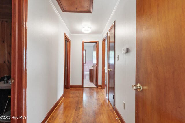 corridor featuring attic access, ornamental molding, light wood finished floors, and baseboards