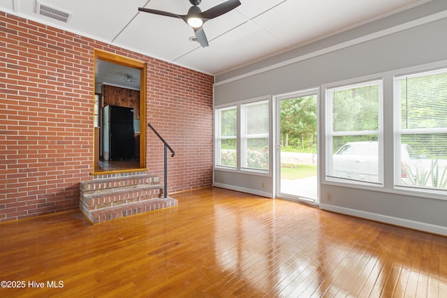 unfurnished living room featuring ceiling fan, visible vents, brick wall, and wood-type flooring