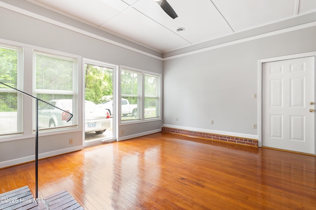 empty room with ceiling fan, crown molding, visible vents, baseboards, and hardwood / wood-style flooring