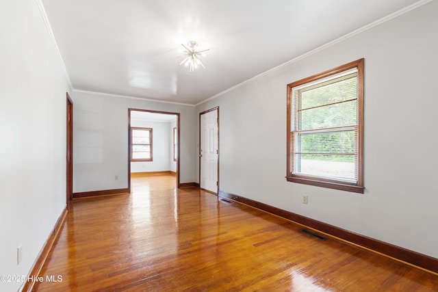 empty room featuring crown molding, visible vents, hardwood / wood-style floors, and baseboards