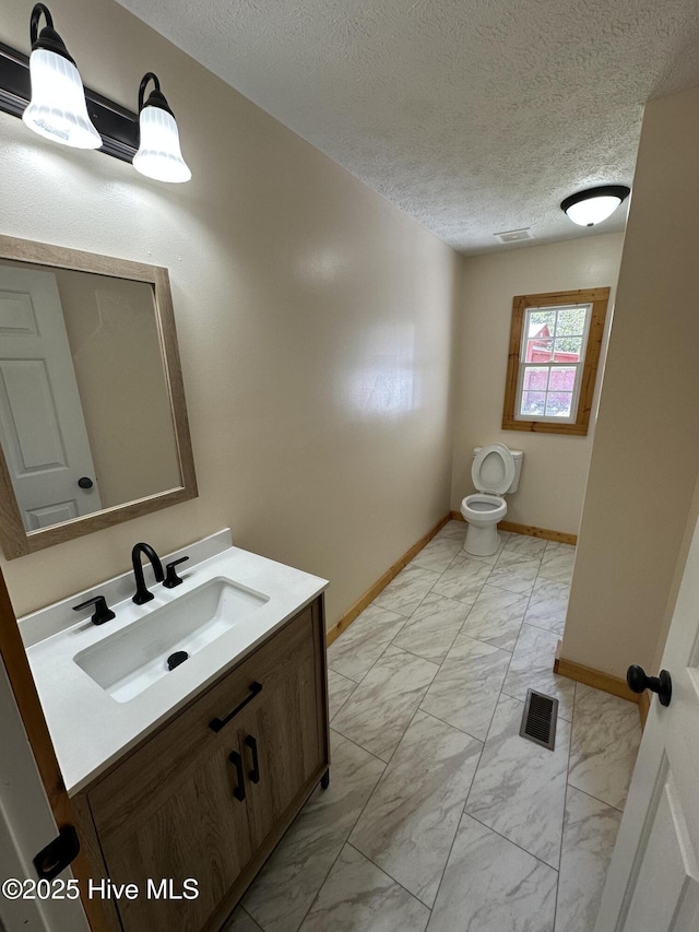 half bathroom with toilet, vanity, marble finish floor, baseboards, and visible vents