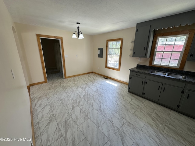 kitchen featuring electric panel, baseboards, dark countertops, a sink, and an inviting chandelier