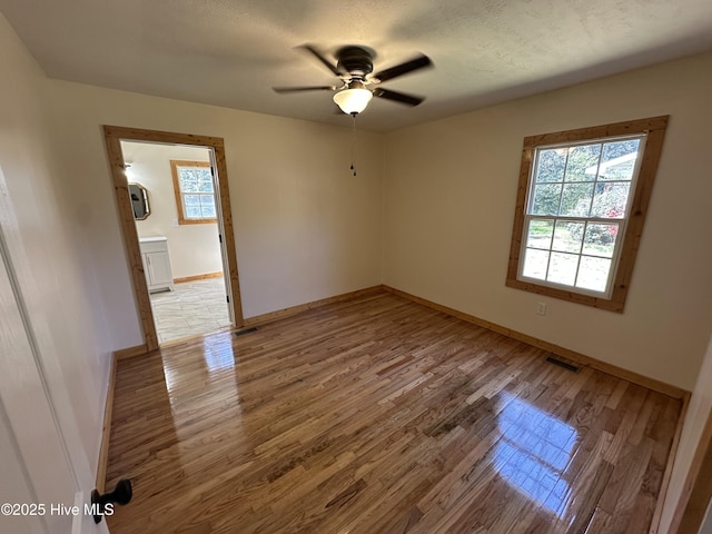 empty room with baseboards, light wood-type flooring, ceiling fan, and a textured ceiling