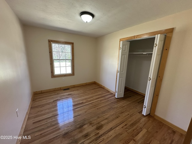 unfurnished bedroom with baseboards, a closet, wood finished floors, and a textured ceiling