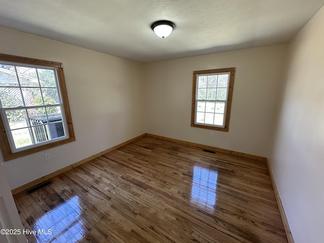 spare room with baseboards, visible vents, and wood finished floors