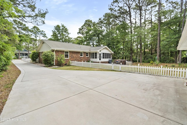 211 E 11th St, Southport, NC 28461 - view of front of house featuring brick siding, a sunroom, concrete driveway, and a fenced front yard