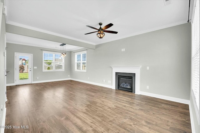 unfurnished living room with a ceiling fan, crown molding, dark wood finished floors, baseboards, and a glass covered fireplace