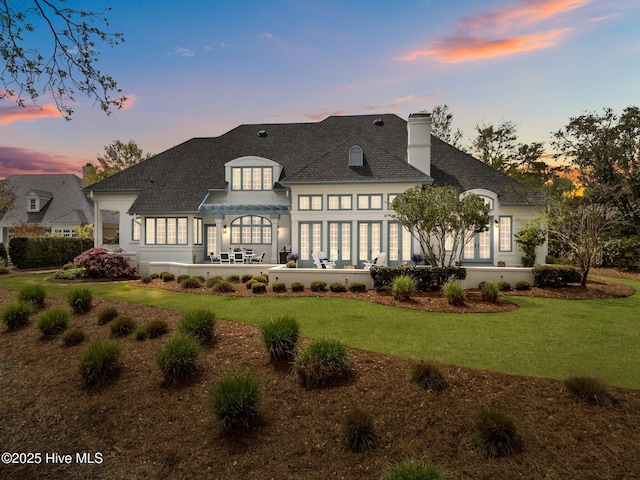 605 Dundee Dr, Wilmington, NC 28405 - back of house at dusk with a chimney, a lawn, a patio area, and roof with shingles