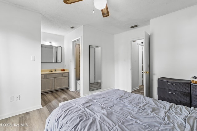 bedroom with a sink, wood finished floors, a textured ceiling, ensuite bath, and visible vents