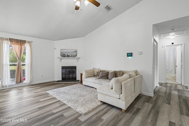 living area with visible vents, a ceiling fan, dark wood-type flooring, a glass covered fireplace, and vaulted ceiling