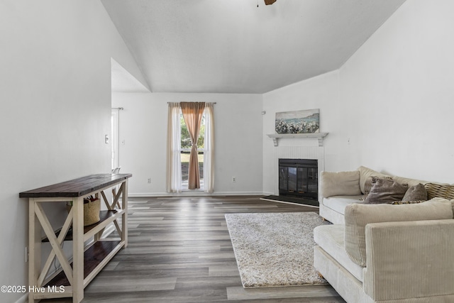 living room featuring dark wood-style floors, lofted ceiling, a fireplace, and baseboards