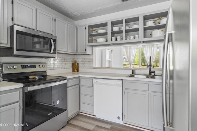 kitchen with light countertops, a sink, appliances with stainless steel finishes, and open shelves