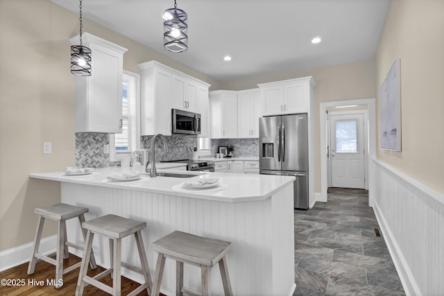 kitchen featuring white cabinets, a peninsula, a breakfast bar, appliances with stainless steel finishes, and a sink