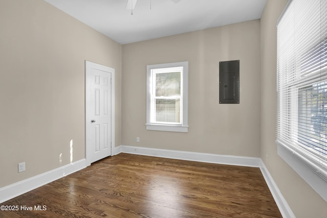 spare room featuring electric panel, baseboards, ceiling fan, and dark wood finished floors