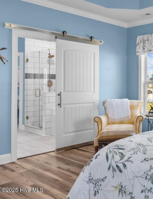 bedroom featuring a barn door, connected bathroom, crown molding, and wood finished floors
