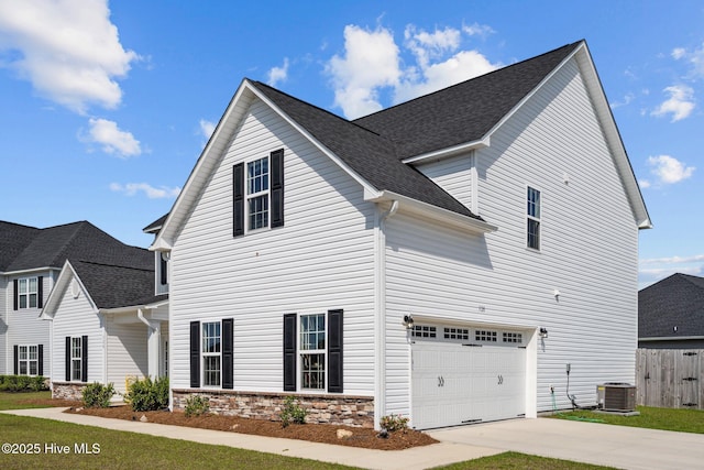 view of side of property with driveway, fence, an attached garage, central AC, and a shingled roof