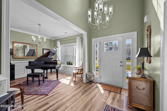 entryway with wood finished floors, a towering ceiling, ornamental molding, and a notable chandelier