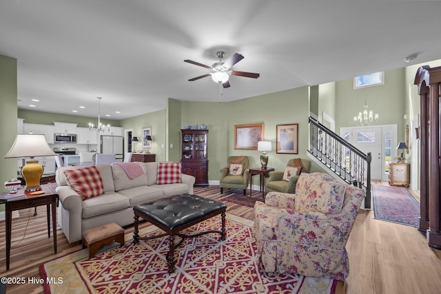 living room featuring light wood finished floors, stairs, ceiling fan with notable chandelier, and recessed lighting