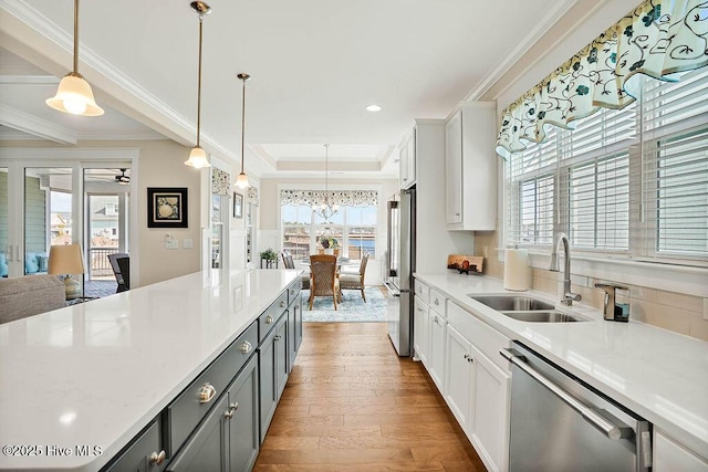 kitchen with a sink, light countertops, stainless steel appliances, wood finished floors, and pendant lighting